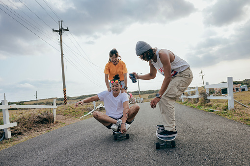 Three Asian skateboarding enthusiasts are playing together outdoors, exchanging skills with each other, and using smartphones to take photos and videos of each other's movements.