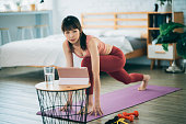 A female Asian is exercising at home, using a tablet for online training courses.