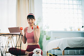 An Asian woman is exercising at home, using a tablet for online training courses, with her pet dog keeping her company by her side.