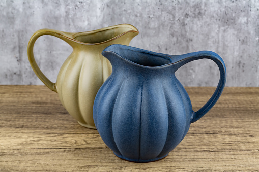 Two ancient style jugs on wooden table on grey wall background.