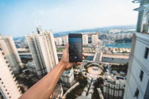 A man holding a mobile phone is filming city scenery at night