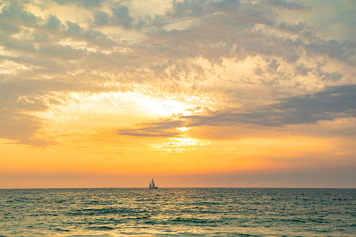 The silhouette of a sailboat on the horizon on the ocean.