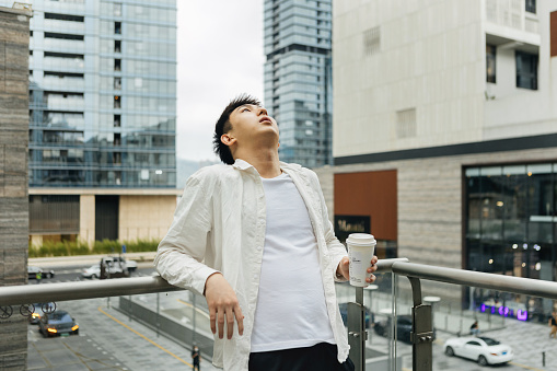 On a cloudy day in Shangcheng, Shenzhen City, Guangdong Province, a male businessman rested on a balcony outside the company, drinking coffee - drinking a cup of coffee after work to promote health and work life balance