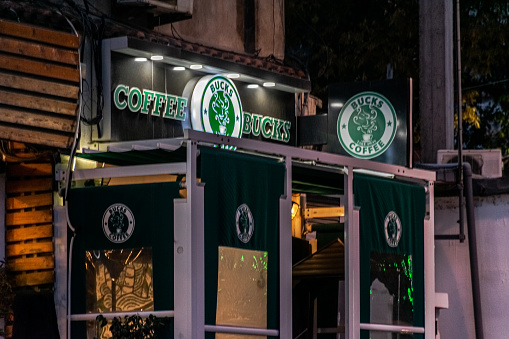 Algiers, Algeria - December 10, 2022: A coffee shop facade in the main road street of Val D'Hydra by night. A brand logo named Coffee Bucks having a big similitude with the Starbucks sign.