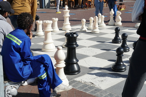 Cape Town, South Africa, 03 22 2023, Local players enjoy a game of street chess with giant figures on the Waterfront in Cape Town South Africa. Some other visitors sitting and observing.