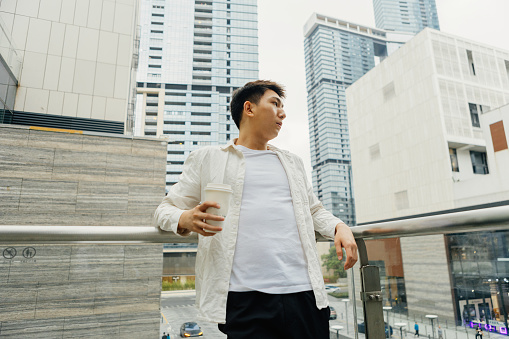 On a cloudy day in Shangcheng, Shenzhen City, Guangdong Province, a male businessman rested on a balcony outside the company, drinking coffee - drinking a cup of coffee after work to promote health and work life balance