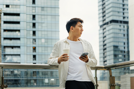 On a cloudy day, a male businessman is resting on a coffee break on the balcony outside the company - drinking a cup of coffee after work, promoting health, work life balance