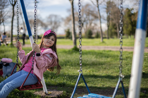 Cheerful little girl is enjoying the spring in the park. She is having fun on the swing.
