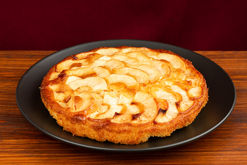 Apple pie on black plate on brown board. Red background. Side horizontal view.