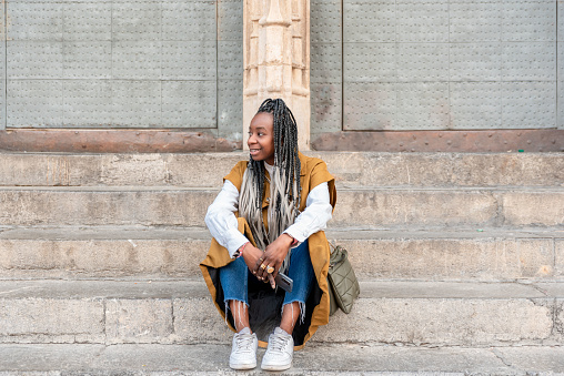 smiling African American woman with braids sitting on stairs in city