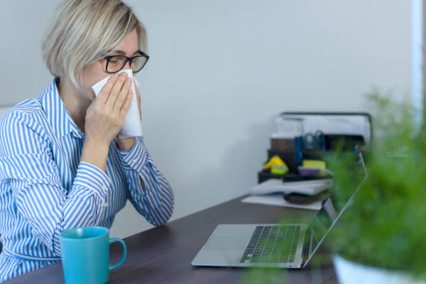 istock A woman blows her nose with a white napkin while sitting at the workplace. 1480100202