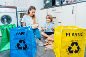Mother is teaching kid how to recycle help the boy aware environmental importance - mom educates son sort garbage into different bins on kitchen. Family sorting garbage at home. Concept of recycling.