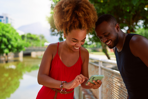young afro black brazilian heterosexual couple using a cell phone and having fun outdoors in a park in Ipanema, Rio de Janeiro