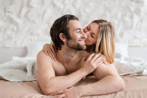 pareja joven y cariñosa acostada junta en la cama, abrazándose y besándose después de hacer el amor. concepto de relación íntima - sexo y reproducción fotografías e imágenes de stock