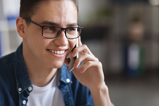 Close Up Portrait Of Millennial Handsome Man Wearing Eyeglasses Talking On Mobile Phone Indoors, Young Cheerful Guy Having Pleasant Conversation, Stylish Male Looking Away And Smiling, Copy Space