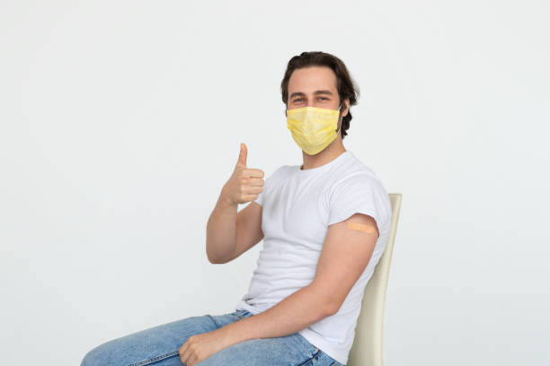 istock Smiling young caucasian man in protective mask with band-aid on shoulder after vaccination shows thumb up 1480107300
