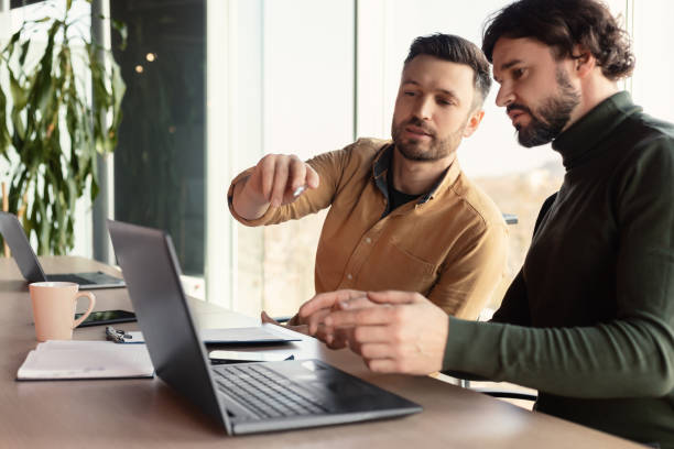 istock Serious employee speaking to his male colleague at company office, using laptop pc, discussing common business project 1480107607