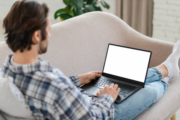 istock Millennial caucasian guy with stubble sits on sofa typing on laptop with blank screen in living room interior 1480107617