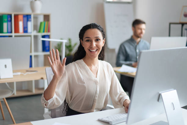 istock Happy young woman working on modern computer, smiling and waving at camera in open space office 1480107685