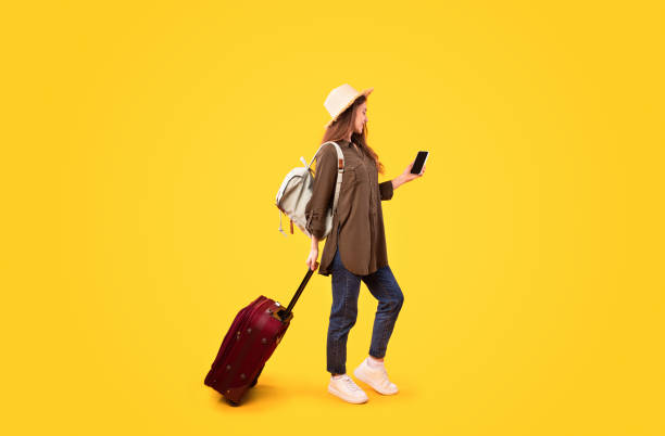 istock Tourist Lady With Suitcase Using Phone Booking Tickets, Yellow Background 1480107785