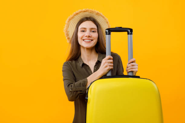 istock Cheerful Lady Tourist Posing With Suitcase Wearing Hat, Yellow Background 1480108174