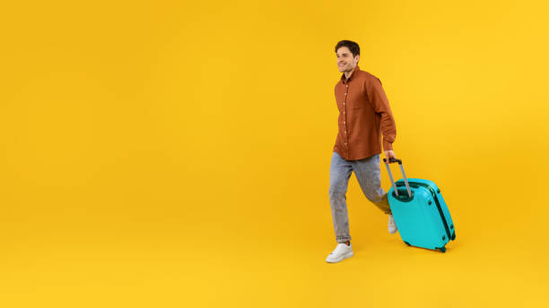 istock Happy Tourist Guy Walking With Blue Suitcase Over Yellow Background 1480108457