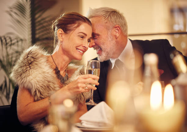 女性、男性、夕食、パーティー、レストランでささやき、笑顔、幸せ、ゴシップで夜に祝う。新年、高級レストラン、ガライベント、シャンパン、会話、ロマンチックな秘密の愛 - whispering couple discussion smiling ストックフォトと画像