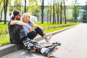 Adult hipster couple with longboard and roller skate sitting in park