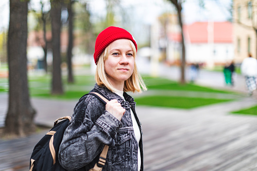 Young adult woman portrait outdoors in red knit hat, spring time, public park