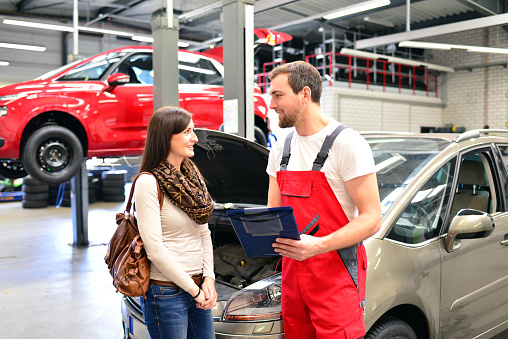 customer service in a garage - mechanic and woman discuss the repair of a vehicle