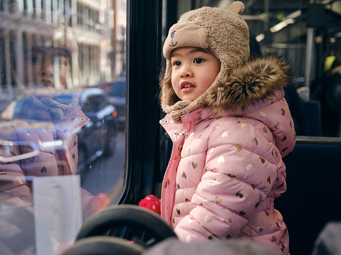 A three year old multiracial girl looking out the window of a light rail train in a downtown area of a city.