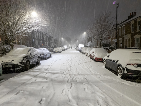 London. UK.12.11.2022. First snowfall in the capital at night blanketing the street, cars and trees in a suburb.
