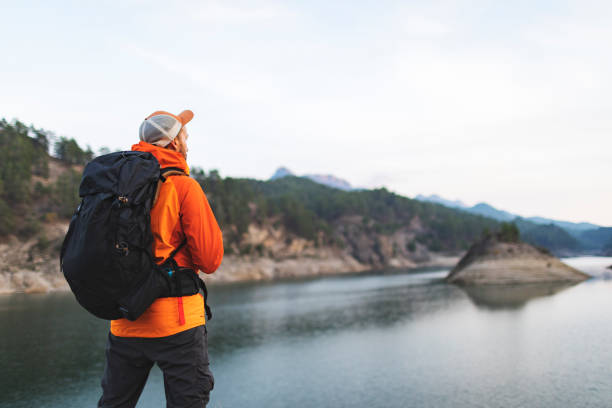 Male backpacker hiking in mountains near lake, resting and looking at view