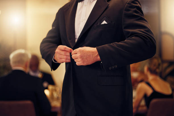 suit, formal and man tie the button of his jacket at a fancy dinner, party or event banquet. classy, elegance and male fixing blazer of his elegant outfit at classic supper, celebration or gathering. - high society men tuxedo party imagens e fotografias de stock