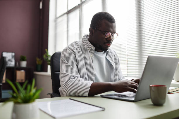 istock Focused black man using laptop working at desk in office wearing casual clothes 1480122935