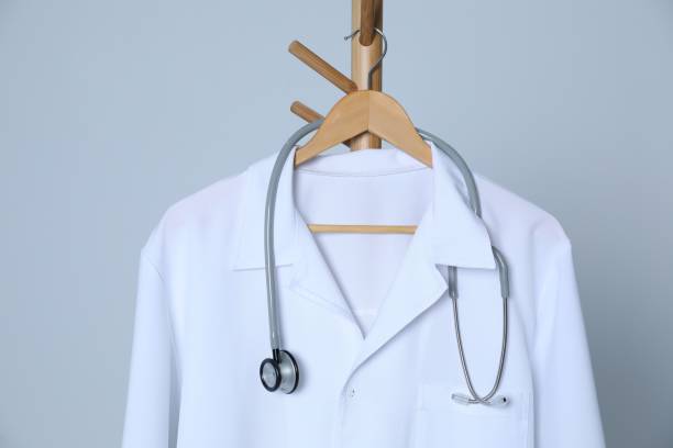 istock Medical uniform and stethoscope hanging on rack against light grey background 1480126774