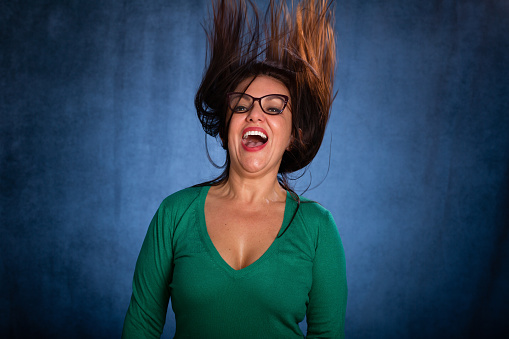 Woman in her 40's portrait. She is cheerfully jumping and looks to the camera smiling. She is happy and excited in the portrait. She wears a green top and reading glasses.