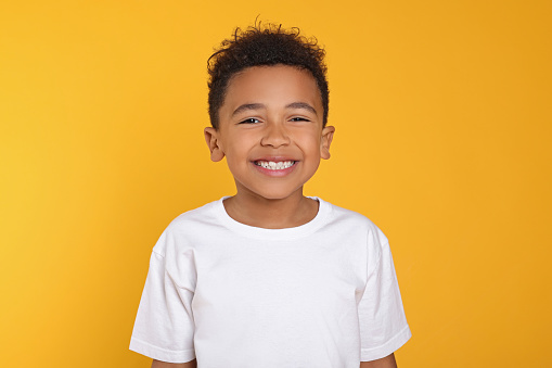 Portrait of cute African-American boy on yellow background