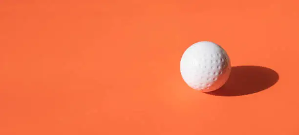 Photo of White dimple hockey ball and golf ball on orange color background. Professional sport concept