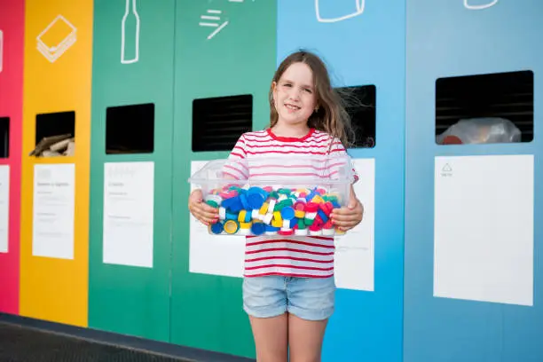 Girls holding container with plastic bottle caps. Kids collecting littered plastic bottlecaps and putting in recycling bin. Sustainble lifestyle concept.