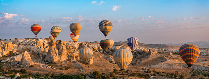 Colorful hot air balloons under rocky landscape of natural formations at sunrise in Cappadocia, central Turkey. Web banner header.
