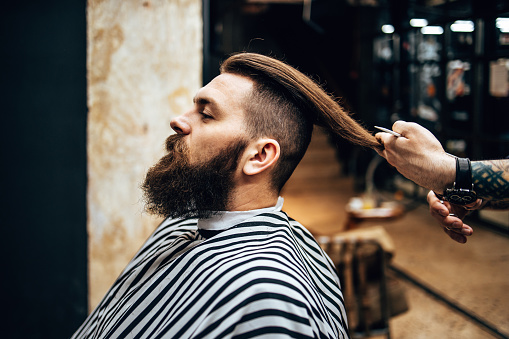 Handsome middle age man receiving hair cutting and styling treatment in a vintage barber shop.