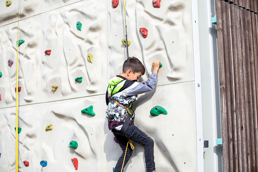 Boy climbing a climbing wall. The model is a 7 year old boy. The model is climbing the wall with the safety rope in the amusement park.