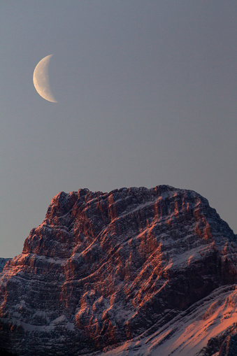 A view of the waxing crescent moon over Mount Lougheed in the Rocky Mountains of Alberta, Canada.