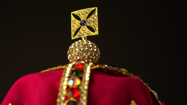 Extreme macro close up of the top of ceremonial coronation diamond crown made of gold and red royal soft velvet material. Black background. Slow rotation motion. 4k, uhd.