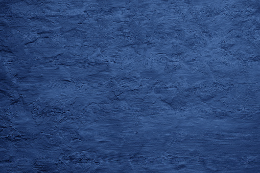 Toned painted concrete wall with plaster. Dark blue vintage texture background with space for design. Close-up. Rough brush strokes. Grungy, grainy, uneven surface. Empty.