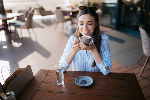 Smiling young woman having a cup of coffee at restaurant. Happy female enjoying a coffee at a outdoor cafe.