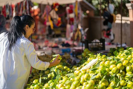 Candid photo of mature adult woman shopping in farmer's market. She is choosing vegetables on market stall. Shot under daylight. Selective focus on model.