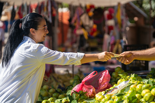 Close up photo of two hands exchanging Turkish paper Lira in farmer's market. Green vegetables are seen on the background. Selective focus on hands. Shot in outdoor with a full frame mirrorless camera.