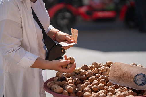 Close up photo of two hands exchanging Turkish paper Lira in farmer's market. Green vegetables are seen on the background. Selective focus on hands. Shot in outdoor with a full frame mirrorless camera.